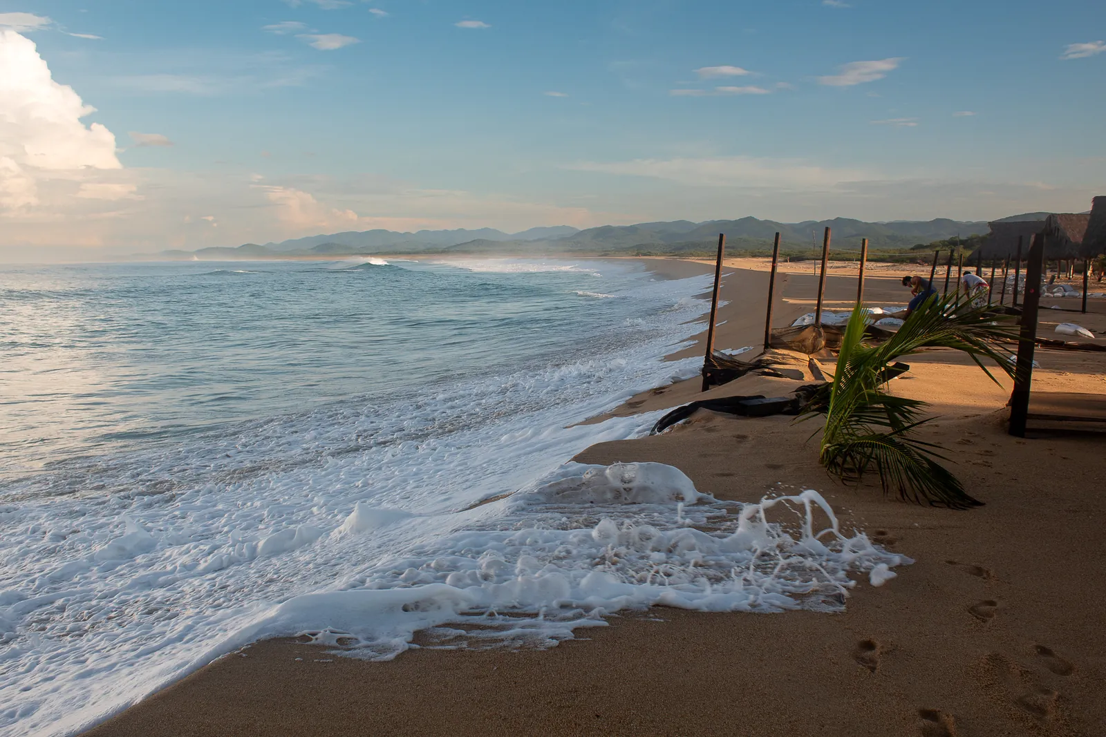 La playa abierta de Chimo al amanecer, con palapas y la sierra al fondo